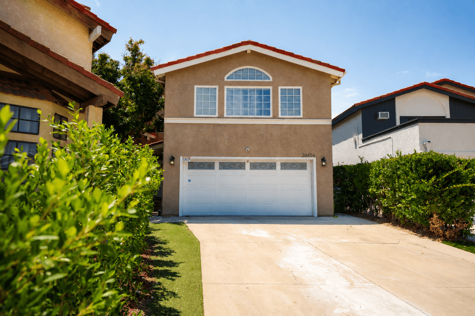 Exterior of a two-story residence with a driveway and garden hedges.