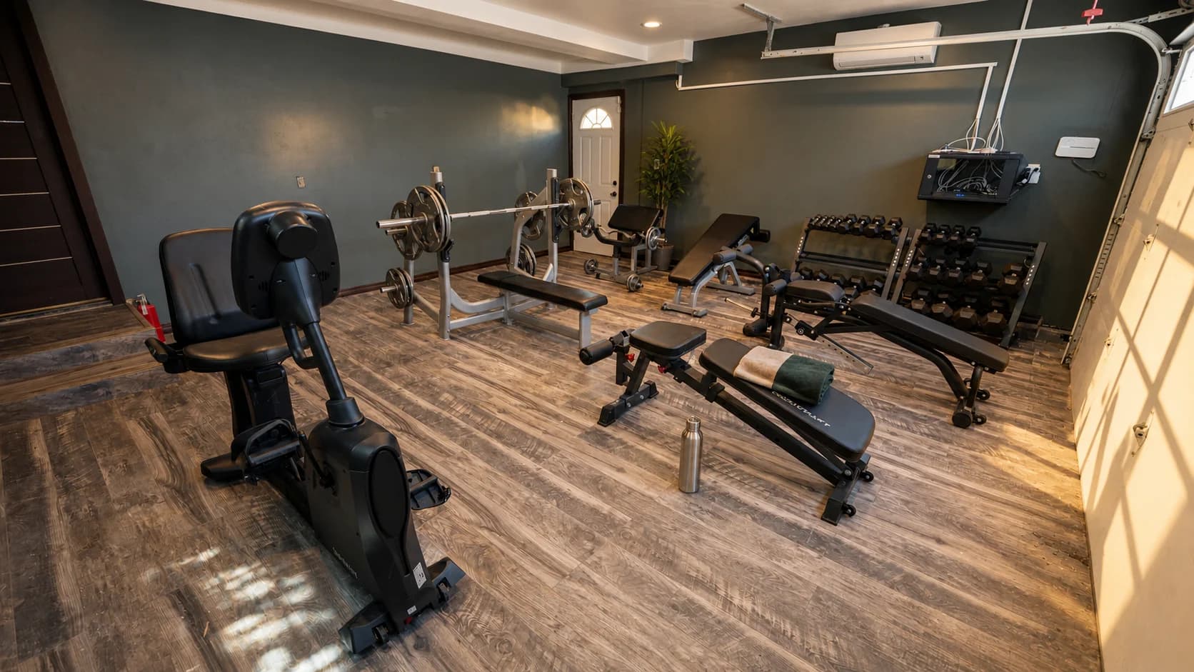 Home gym with squat rack and dumbbells under dark walls.