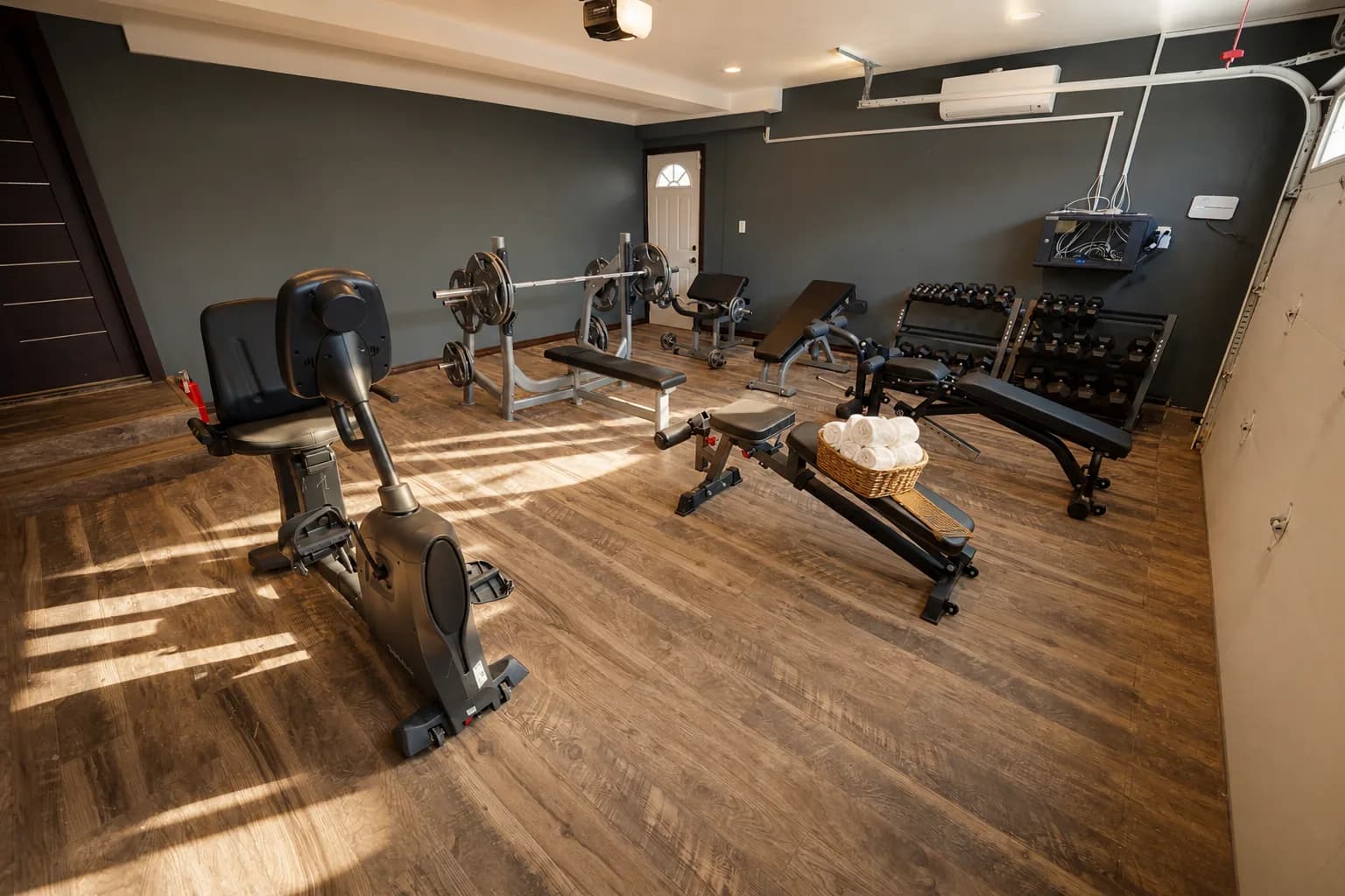 The residence fitness room at Providence Detox, benches and dumbbells on a wood floor under dark walls.