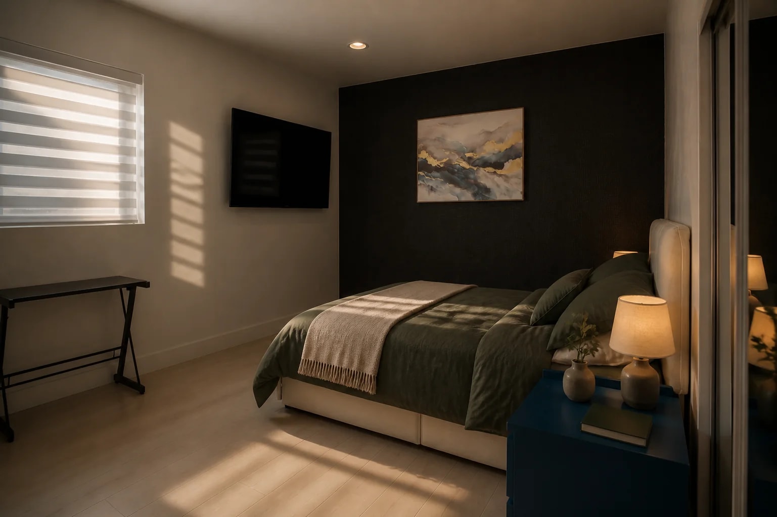 A guest bedroom at dusk, olive bedding turned back beside a lit lamp and a dark accent wall.