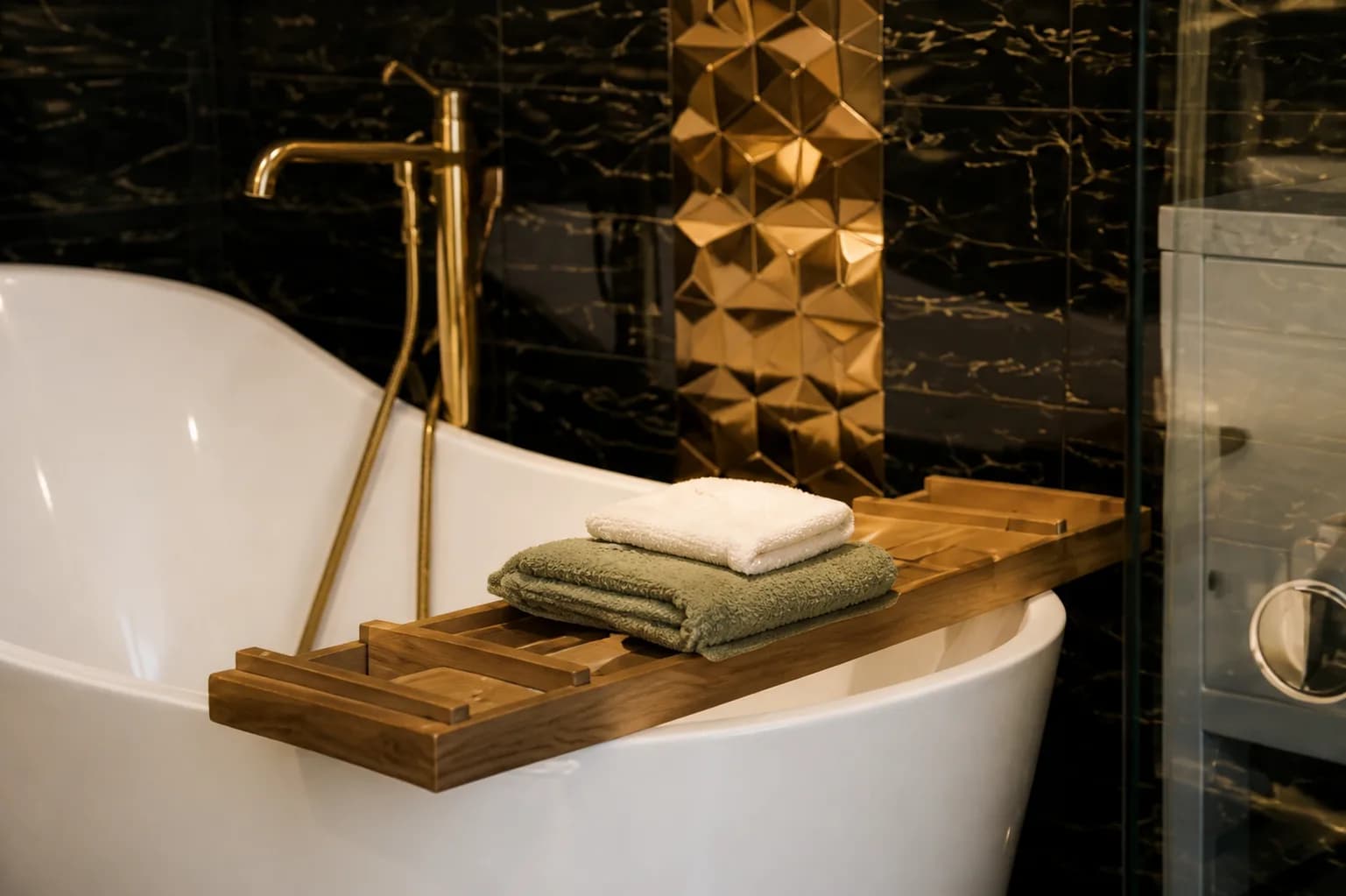 A freestanding tub with a wooden bath tray and folded towels against dark marble at Providence Detox.