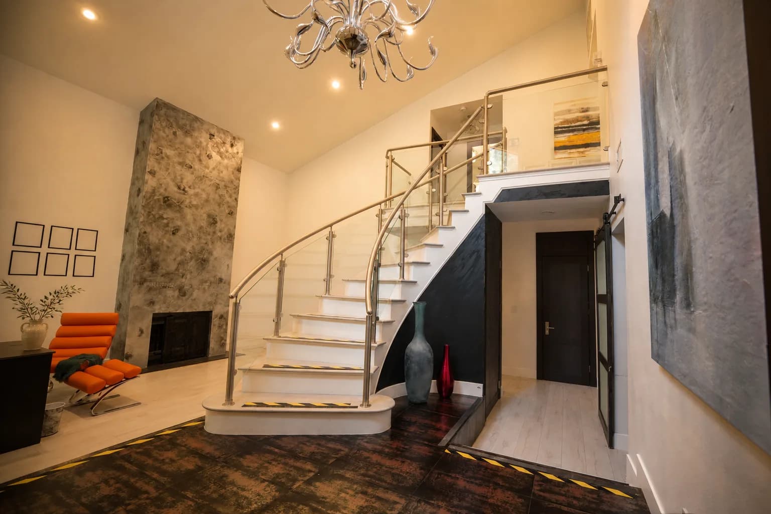 The entry hall at Providence Detox, a curved staircase and chandelier beside the stone fireplace.